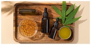 CBD oil products on a wooden tray with hemp leaf – capsules, tinctures, balm and glass bottle