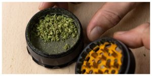 hand holding a black and orange four piece grinder with some weed on a wooden table