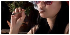 asian girl smoking a joint, cannabis plant in the background