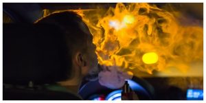 a man smoking a vape in the car at nighttime, lots of smoke around him and an orange light outside