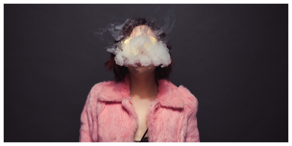 girl in pink fur coat exhaling smoke, grey background