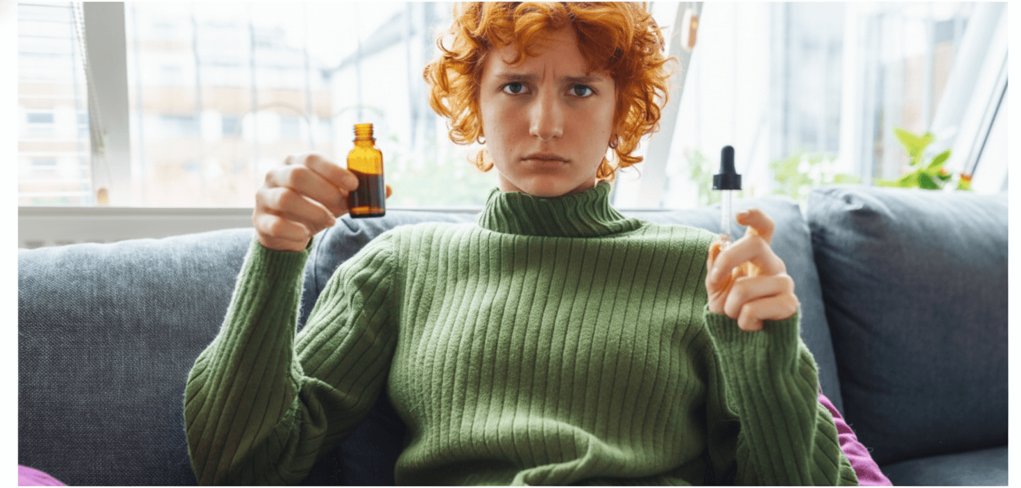 a girl seating on a sofa holding a cbd oil bottle and an oil dropper, wondering if you can overdose on cbd