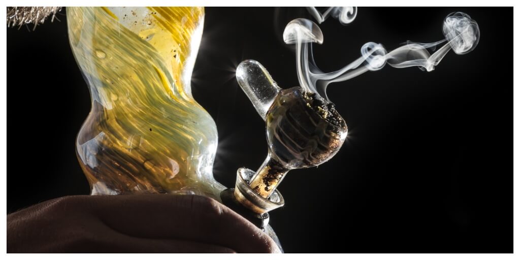 man smoking a glass bong in dark, comparing silicone bongs vs glass bongs